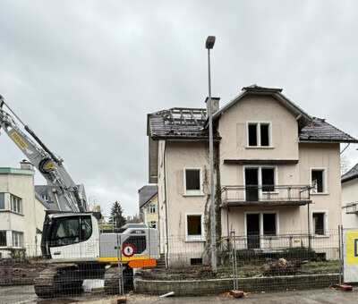 Gebaeude im Abbruch mit Bagger neben einem intakten Nachbarhaus