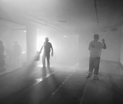 Schwarzweiss-Aufnahme zweier Personen, die durch einen dunklen, lichtdurchfluteten Gang gehen
